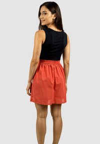 Top negro sin mangas con escote redondo, combinado con una falda de cintura elástica coral, que presenta una textura suave y un tejido fluido.