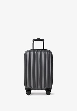 Twarda czarna walizka na czterech kółkach z wysuwaną teleskopową rączką, stojąca pionowo na białym tle.