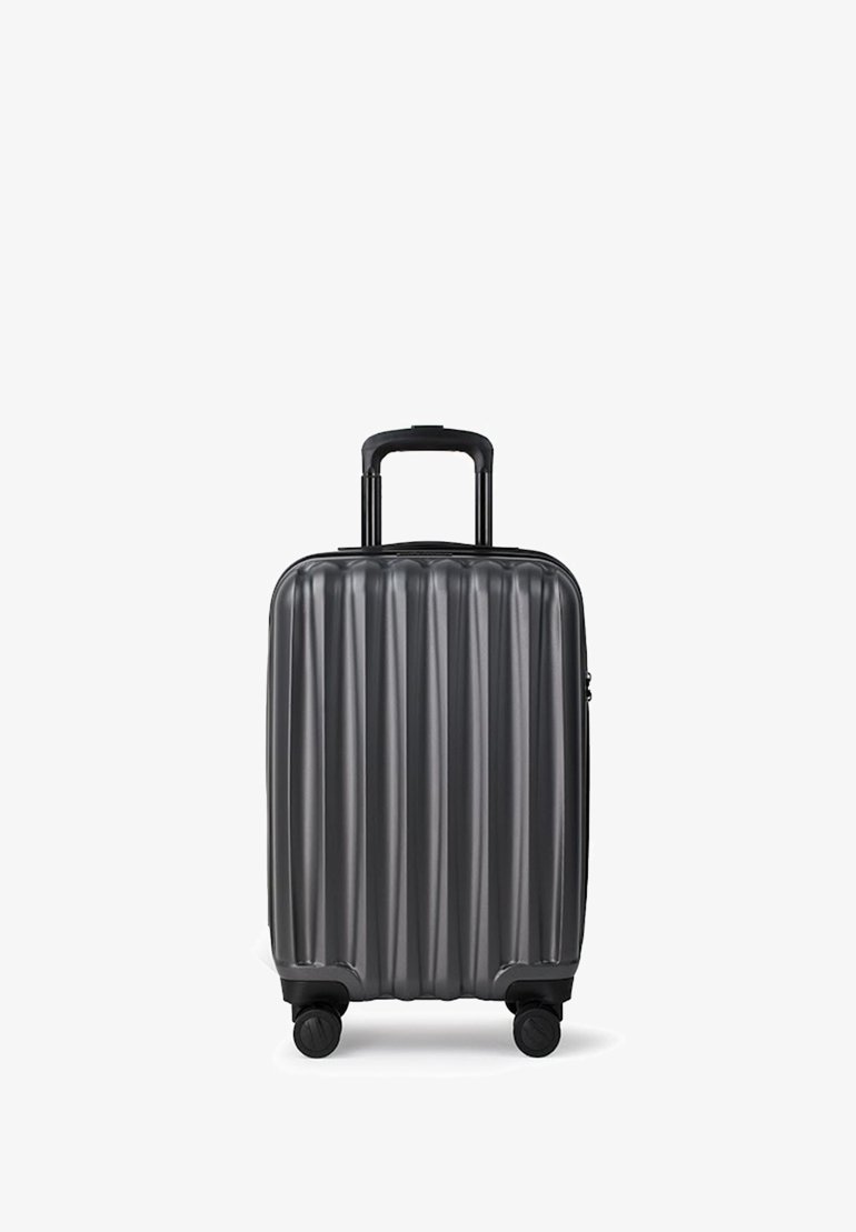 Twarda czarna walizka na czterech kółkach z wysuwaną teleskopową rączką, stojąca pionowo na białym tle.