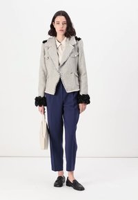 Grijze tweed blazer met zwarte bontaccenten op de manchetten, dubbel geknoopt met zilveren knopen, gecombineerd met marineblauwe broek en zwarte loafers.