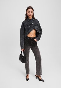 Veste en denim noire raccourcie avec des boutons argentés et des poches, associée à un jean noir taille haute, un sac à main noir et des escarpins à bout pointu.