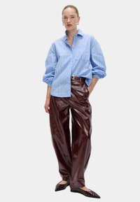 Niebieska koszula z guzikami w paski, z oversize'owymi rękawami, w zestawieniu z błyszczącymi burgundowymi spodniami szwajcarskimi i czarnymi czółenkami z punta, ozdobionymi srebrnymi akcentami.