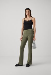 Black tank top with lace detailing, olive green ribbed flared pants, and a silver handbag. Black shoes complete the look.