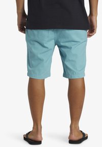 Ljusblå bomullsshorts med en avslappnad passform, uppvikta fållar och sidofickor, tillsammans med svarta flip-flops, vy från baksidan.