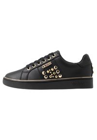 Sneaker nera a basso profilo con occhielli dorati, borchie e il marchio "GUESS" sul lato e sulla suola.