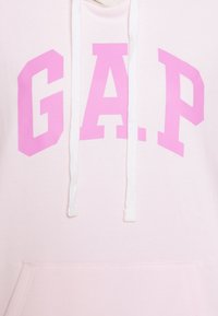 Felpa rosa con una grande e audace grafica "G.A.P." in rosa sul davanti. Presenta cordini bianchi e una tasca a marsupio. Tessuto morbido.
