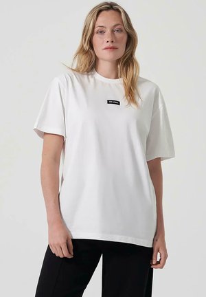 T-shirt blanc en coton avec un col rond et des manches courtes. Présente une petite étiquette noire avec "ON APRIL" sur la zone de la poitrine.