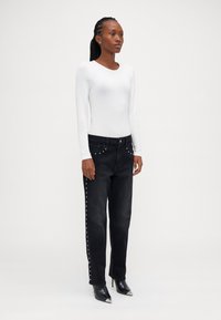 Jeans negri din denim cu studs argintii pe lateral, asortați cu un top alb cu mânecă lungă. Modelul poartă pantofi cu toc ascuțit negri.