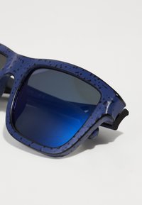Óculos de sol azuis com uma armação púrpura salpicada, lentes retangulares e um tom degradê azul escuro, apresentando um detalhe em borracha preta.
