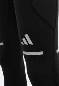 Gros plan sur un legging de sport noir avec logo Adidas réfléchissant et détails de couture.