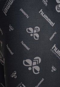 Svarta träningsleggings med en slät textur, med ett upprepat grått logomönster av "hummel" och abstrakta former över tyget.