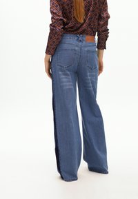 Leveled jeans made of light blue denim, with a navy side panel, stitched details, and a brown leather back patch.