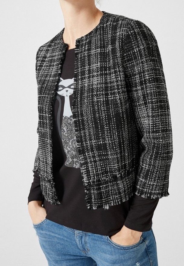 Mustavalkoinen ruudullinen lyhyt takki, jossa on pyöreä kaulus ja repaleiset reunat, kerrostettuna mustan yläosan kanssa, jossa on kissagrafiikka.