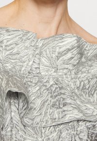 Robe à épaules dénudées avec un motif zèbre texturé argenté et gris, dotée de volants superposés autour de l'encolure et du corsage.