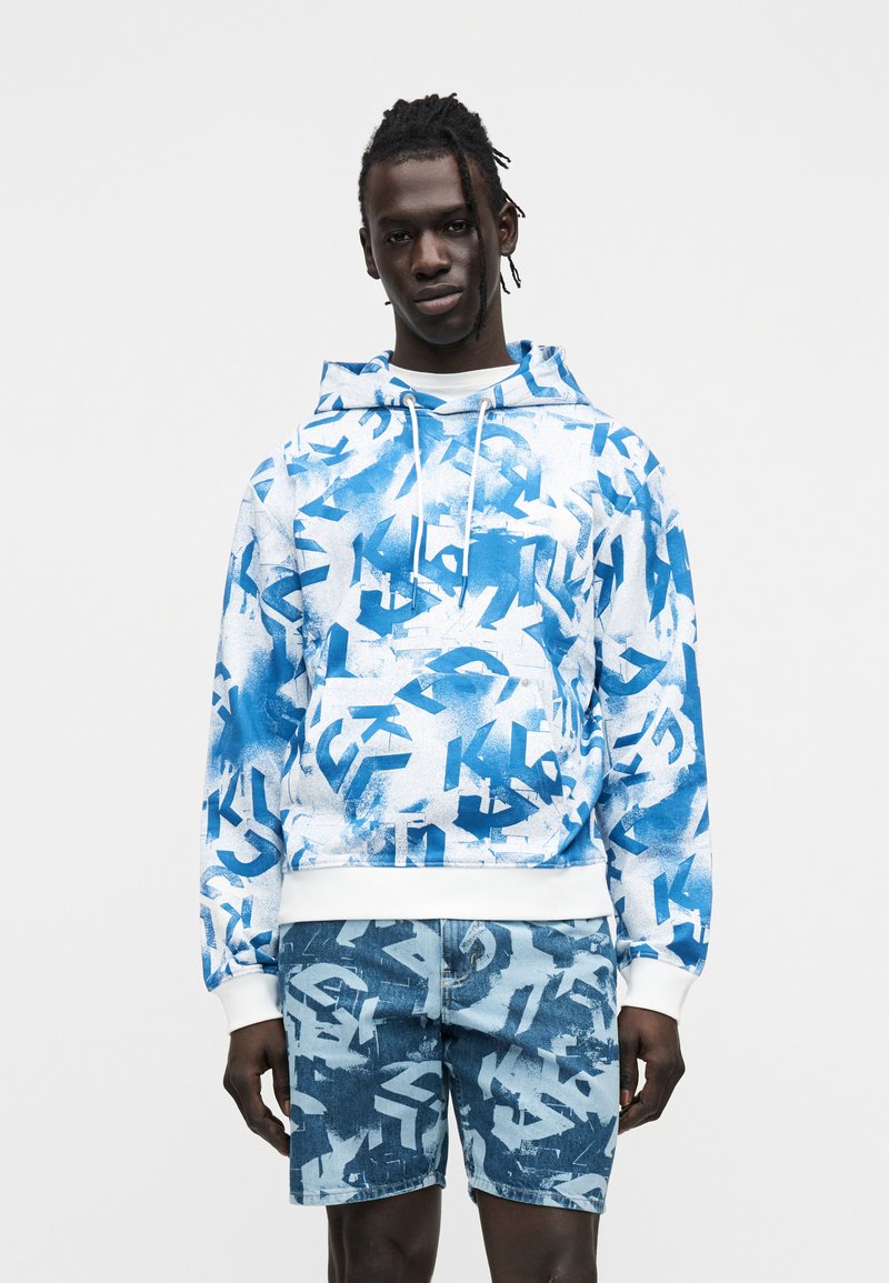 Ελαφρύ μπλε και άσπρο φούτερ με αφηρημένα μοτίβα, με κουκούλα με κορδόνι και ριμπ μανσέτες, συνδυασμένο με ταιριαστά τζιν σορτς.