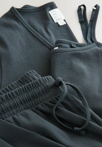 Dark gray ribbed fabric loungewear set, featuring a tank top with thin straps and pants with an elastic waistband and adjustable drawstring.