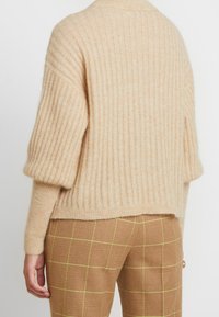 Maglione beige a coste con maniche larghe, realizzato in morbida lana, presenta un orlo posteriore rilassato, che mette in evidenza dettagli in maglia testurizzata.