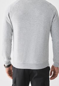 Felpa grigia con finitura texturizzata, maniche raglan lunghe e orlo arrotondato. Tessuto liscio, senza motivi significativi o dettagli aggiuntivi.