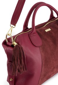 Bordová kabelka s kombinací strukturované kůže a semiše, se zipovým uzávěrem, krátkými uchy a dekorativním střapcem.