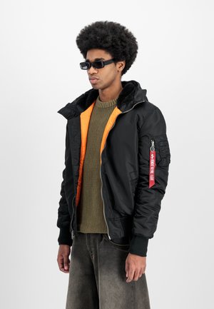 Must must jacket, mille oranž vooder, faux karusnahast krae, tõmblukuga taskud ja punane silt varrukal. Kantud rohelise kudumi sularüü peal.