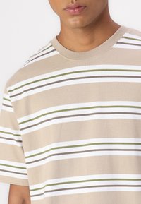 Beige short-sleeve t-shirt with horizontal stripes in white, olive green, and brown. Soft cotton material and a classic crew neckline.