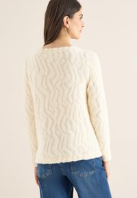 Suéter color crema con un patrón de zigzag texturizado, hecho de material peludo. Cuenta con un escote redondo y mangas largas.