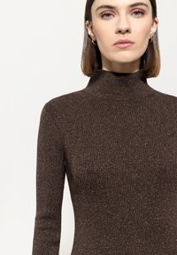 Brauner gerippter Rollkragenpullover aus strukturiertem Material mit metallischen Fäden. Enganliegendes Design mit langen Ärmeln und hohem Kragen.