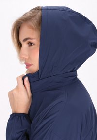 Marinblå zip-up jacka med huva, slätt tyg, elastiska mudd och en nära passform. Har sömnadsdetaljer längs sömmarna.