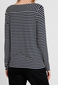 Gestreiftes Langarmoberteil in Marineblau und Weiß mit einem weiten Bootsausschnitt und einer Nahtdetails auf der Rückseite; aus weichem Stoff mit lässiger Passform.