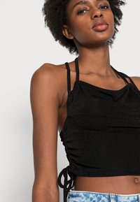 Top preto cropped com lados franzidos ajustáveis e alças finas. Tecido macio e texturizado com um design franzido na parte do busto.