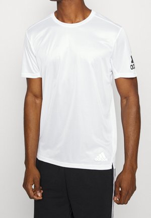 Homme portant un t-shirt Adidas à manches courtes blanc avec logo sur la poitrine gauche et la manche droite, associé à un pantalon noir.
