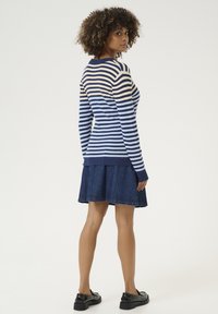 Pruhovaný pletený sveter v námorníckej modrej, krémovej a modrej farbe, skombinovaný s džínsovou sukňou. Má dlhé rukávy a rebrované manžety. Hladká textúra.