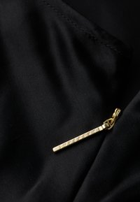 Tissu noir avec une texture lisse, orné d'une tirette dorée. La tirette est gravée avec "SUPERDRY" dans une ligne droite.