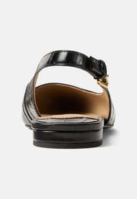 Μαύρο πέδιλο από δερμάτινο δέρμα με λουράκι στο πίσω μέρος, υφή, και χρυσή αγκράφα. Διαθέτει επίπεδη σόλα και φυσική δερμάτινη εσωτερική σόλα.