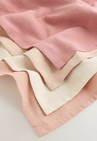 Warstwy materiałów w delikatnym różowym, beżowym i ecru kolorach z widocznymi szwami wzdłuż krawędzi na jasnym tle.