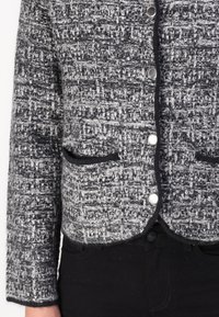 Grå og svart tweed-jakke med teksturert design, med sølvknapper og svarte pipede lommer, med lange ermer og kort skåret.
