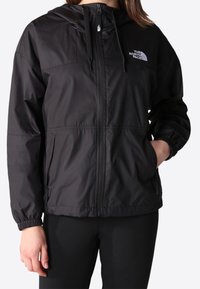Giacca a vento nera con zip frontale, cappuccio, polsini elastici e tasche. Presenta il logo The North Face nella parte superiore sinistra.