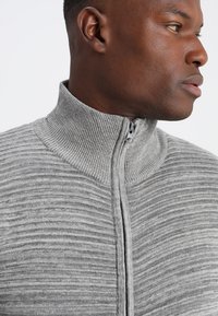 Grau zip-up Pullover mit vertikal gerippter Textur, hohem Kragen und einem glatten Reißverschluss, entworfen für eine taillierte Passform.
