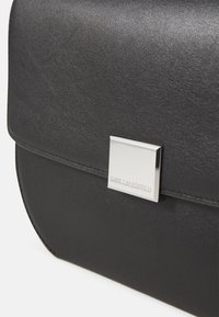 Borsa a tracolla in pelle nera con una texture liscia, dotata di una chiusura quadrata in metallo argentato e logo impresso sul davanti.