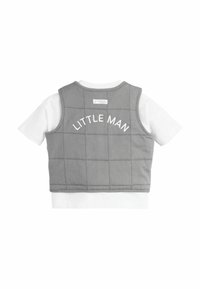 Gilet matelassé gris avec le texte "LITTLE MAN" en blanc, superposé à un t-shirt blanc à manches courtes. Texture de tissu douce.