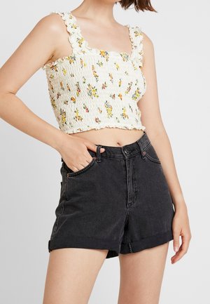 Valkoinen kukkakirjailtu lyhyt toppi, jossa röyhelöreunat, yhdistetty korkeavyötäröisiin mustiin farkkushortseihin, joissa on käännetyt reunat ja etutaskut.