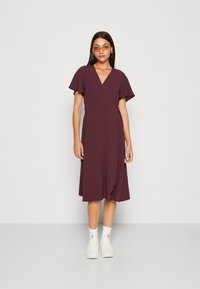 Burgundy wrap dress with short flutter sleeves, knee-length, textured fabric, and a tie detail at the waist. Worn with white sneakers.
