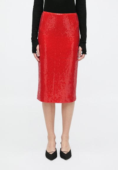 Jupe crayon en sequins rouges avec un design ajusté, longueur mi-mollet et texture lisse. Portée avec un haut noir à manches longues et des talons noirs.