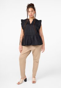 Čierny peplum top s krátkymi volánovými rukávmi a výstrihom do V. Béžové zúžené nohavice a svetlé sandále na blokovom podpätku dotvárajú outfit.