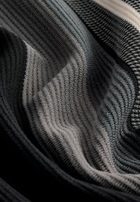 Tissu tricoté à rayures horizontales en noir, gris et une teinte plus claire. Présente une surface douce et texturée avec un motif côtelé.