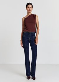 Haut asymétrique bordeaux avec détail drapé ; associé à un jean évasé bleu foncé avec des coutures contrastées et une ceinture à boutons distincte.