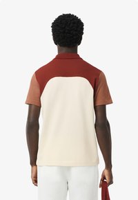Kortärmad polo t-shirt med färgblockdesign i vinröd, beige och brun. Tillverkad av mjukt material med klassisk krage och detalj på baksidan.