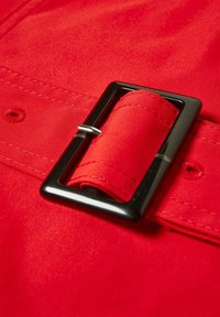 Tela roja resaltada con una hebilla rectangular negra brillante. Textura suave con costuras ajustadas y un lazo para el ajuste del cinturón.