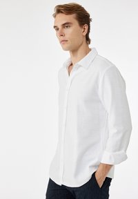 Witte button-up shirt gemaakt van lichtgewicht stof, met een klassieke kraag en opgerolde mouwen, met een eenvoudige, gladde textuur.