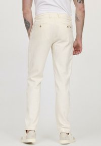 Pantalons en lin beige clair avec une coupe droite, dotés de poches arrière avec des boutons en laiton et un ourlet à revers, assortis de baskets légères.